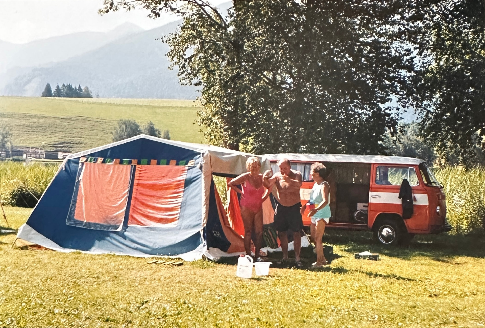 The orange VW T2 set up at a campsite with a tent and folding chairs