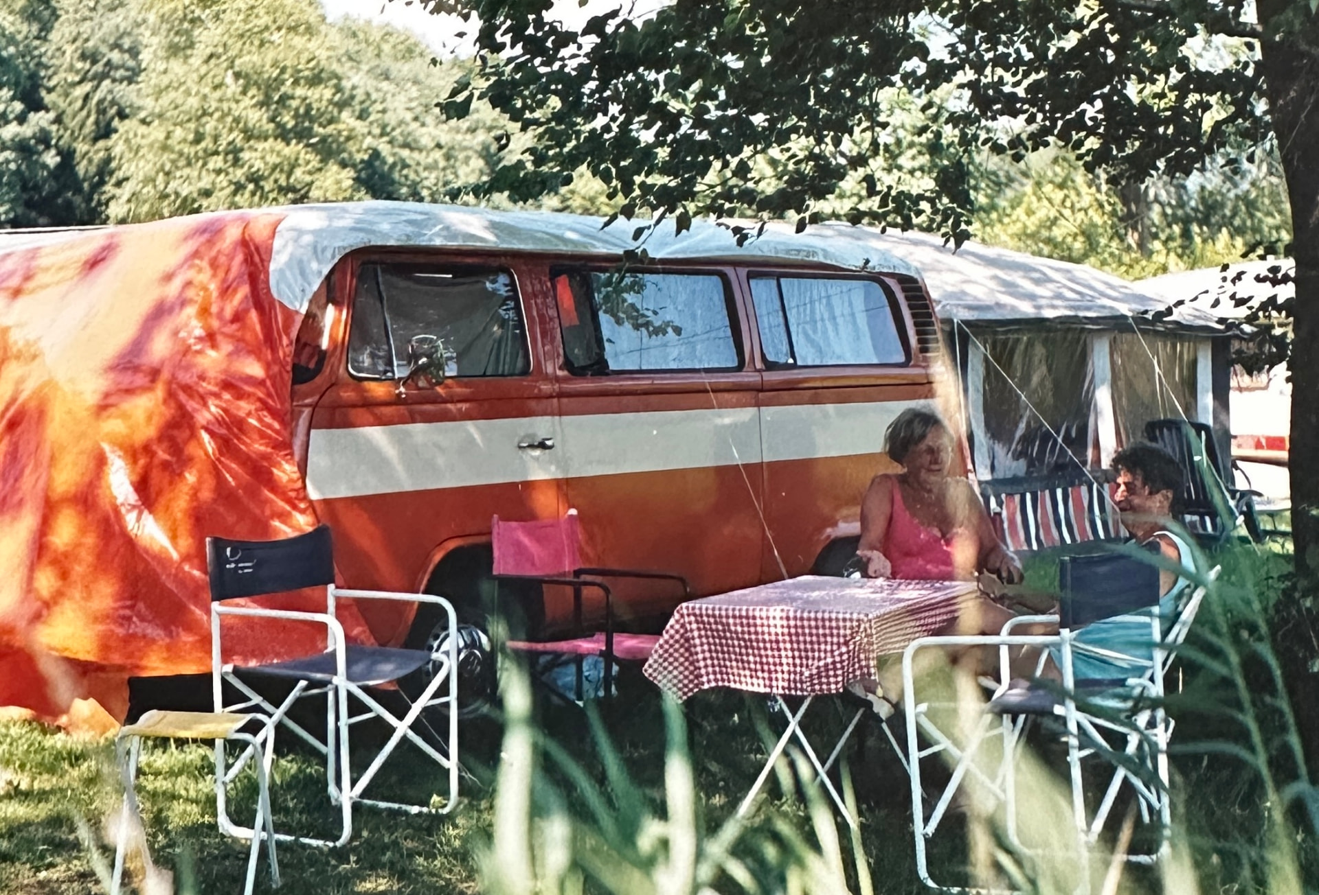 The orange VW T2 with a tent and family members at a campsite