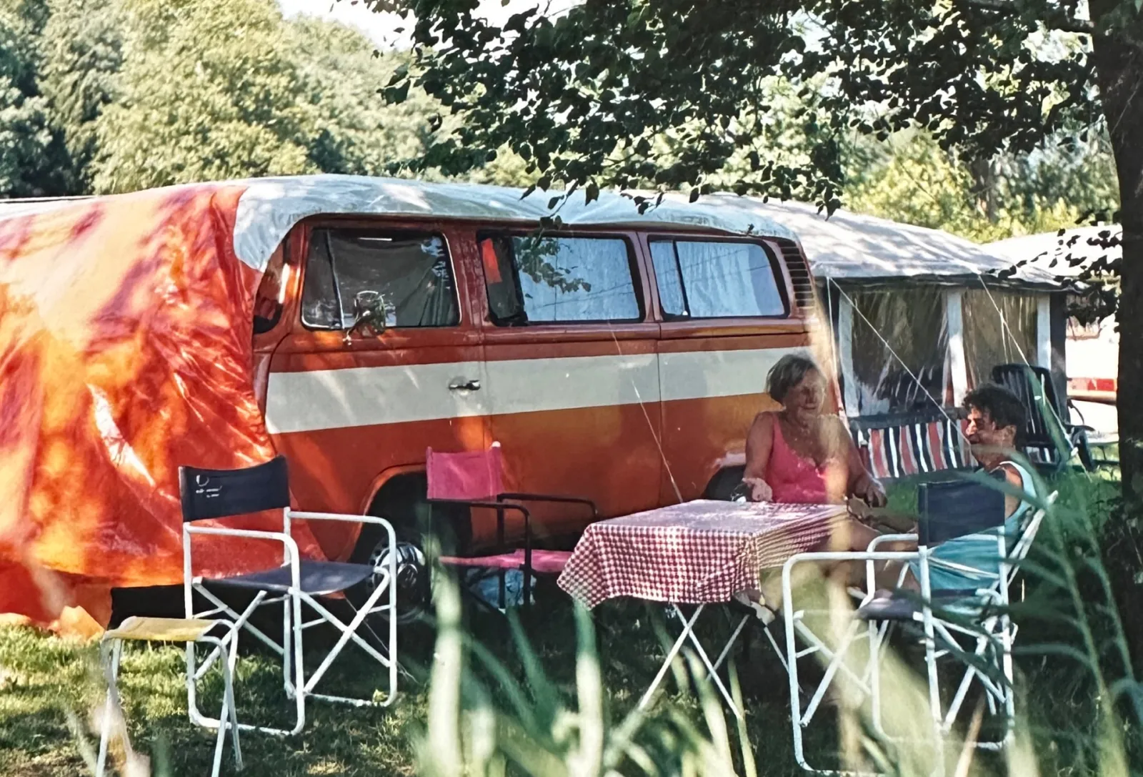 The orange VW T2 with a tent and family members at a campsite