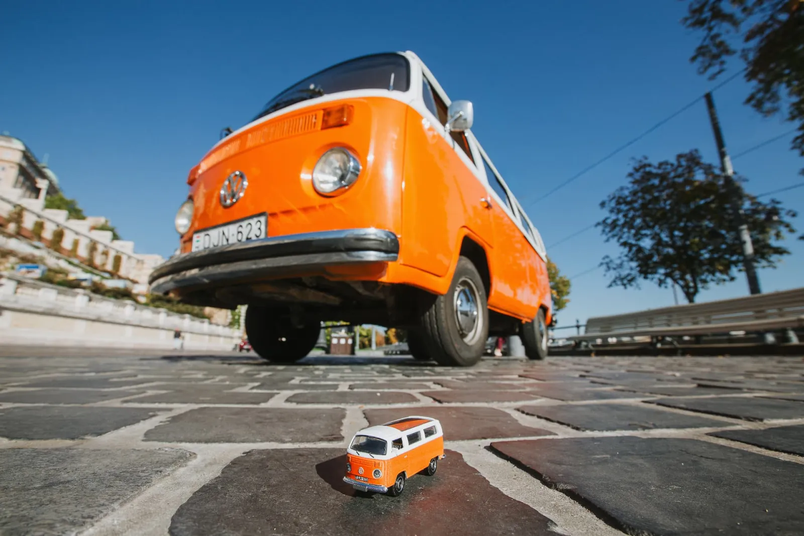 The Matchbox model resting on a cobblestone in front of the full-size orange and white Volkswagen T2 with the DJN-623 plate