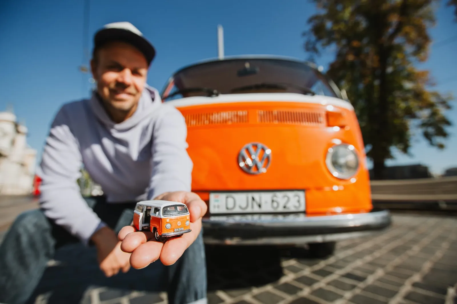 The current owner holding the Matchbox model of his Volkswagen in his open palm, with the real DJN-623 bus directly behind him