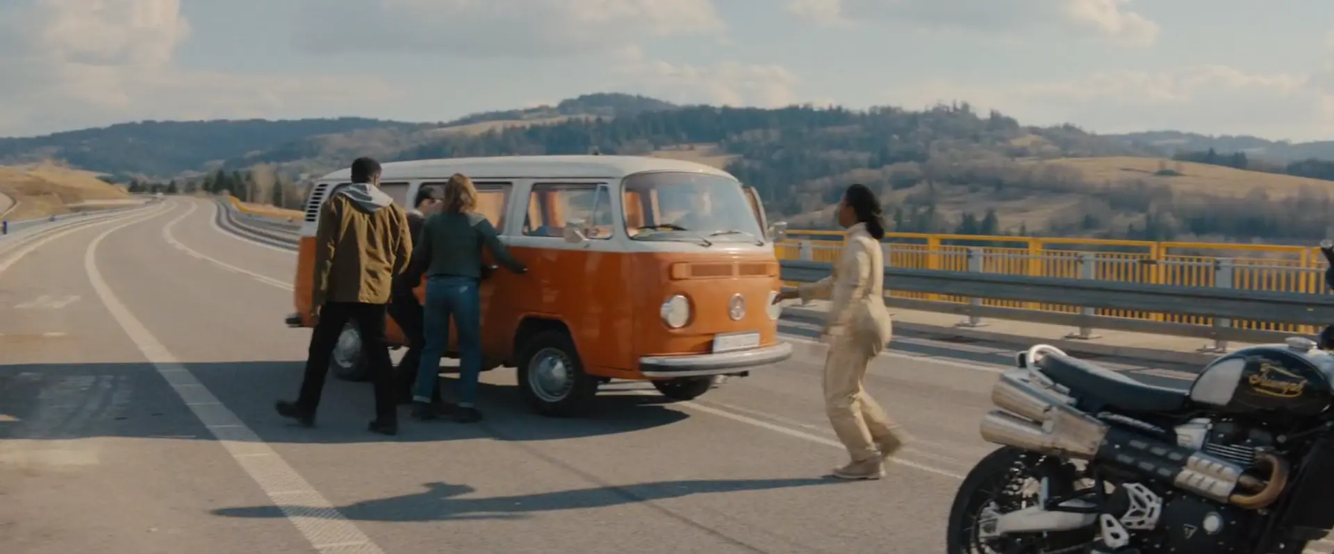The cast stopping the orange VW T2 on the highway bridge, a motorcycle parked in the foreground
