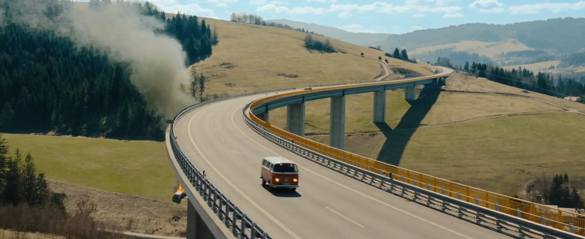 The orange VW T2 driving along a curved concrete viaduct in hilly countryside