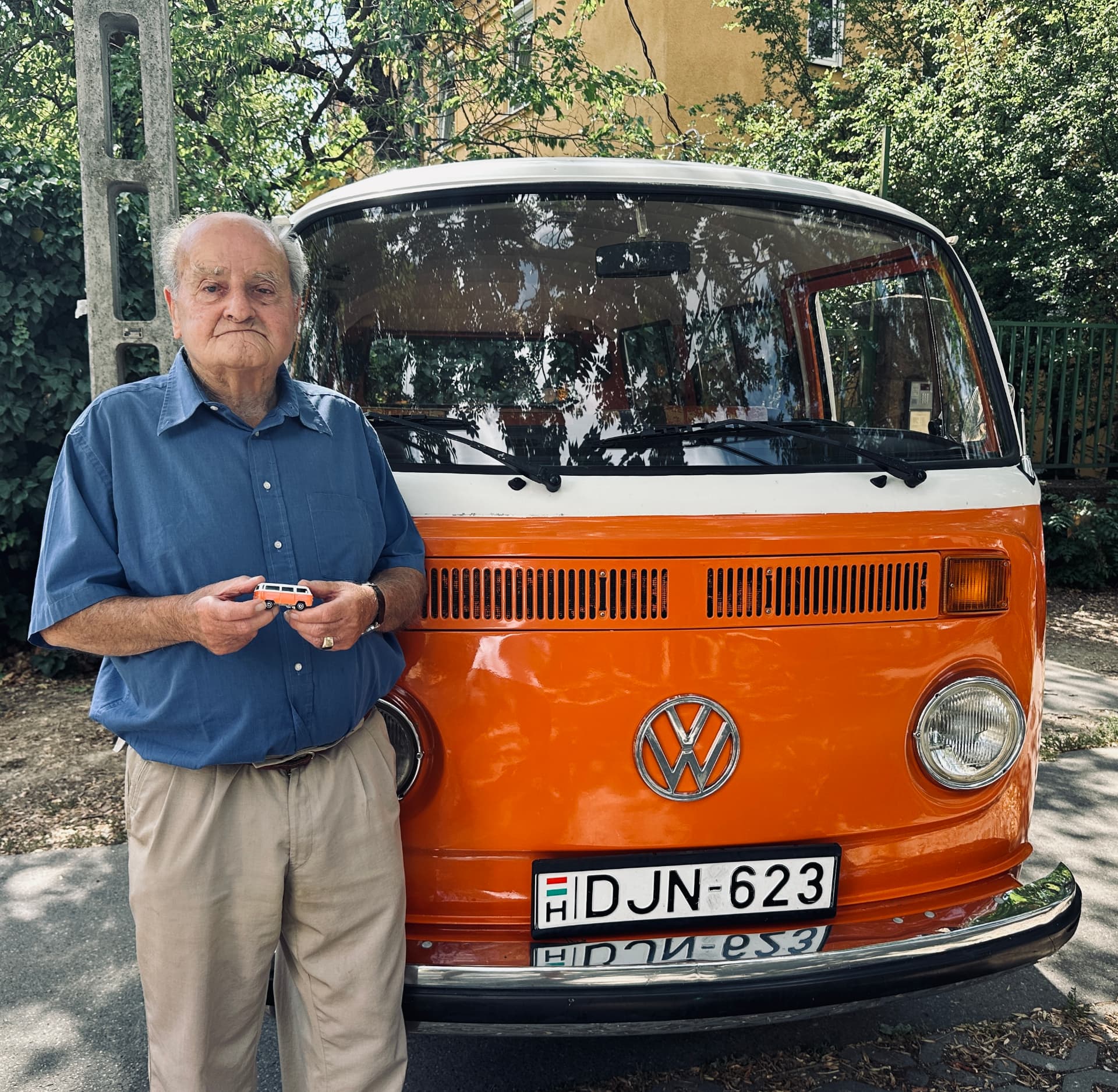 Mr. Thaly standing in front of the real orange VW T2 with the DJN-623 plate, holding the Matchbox model